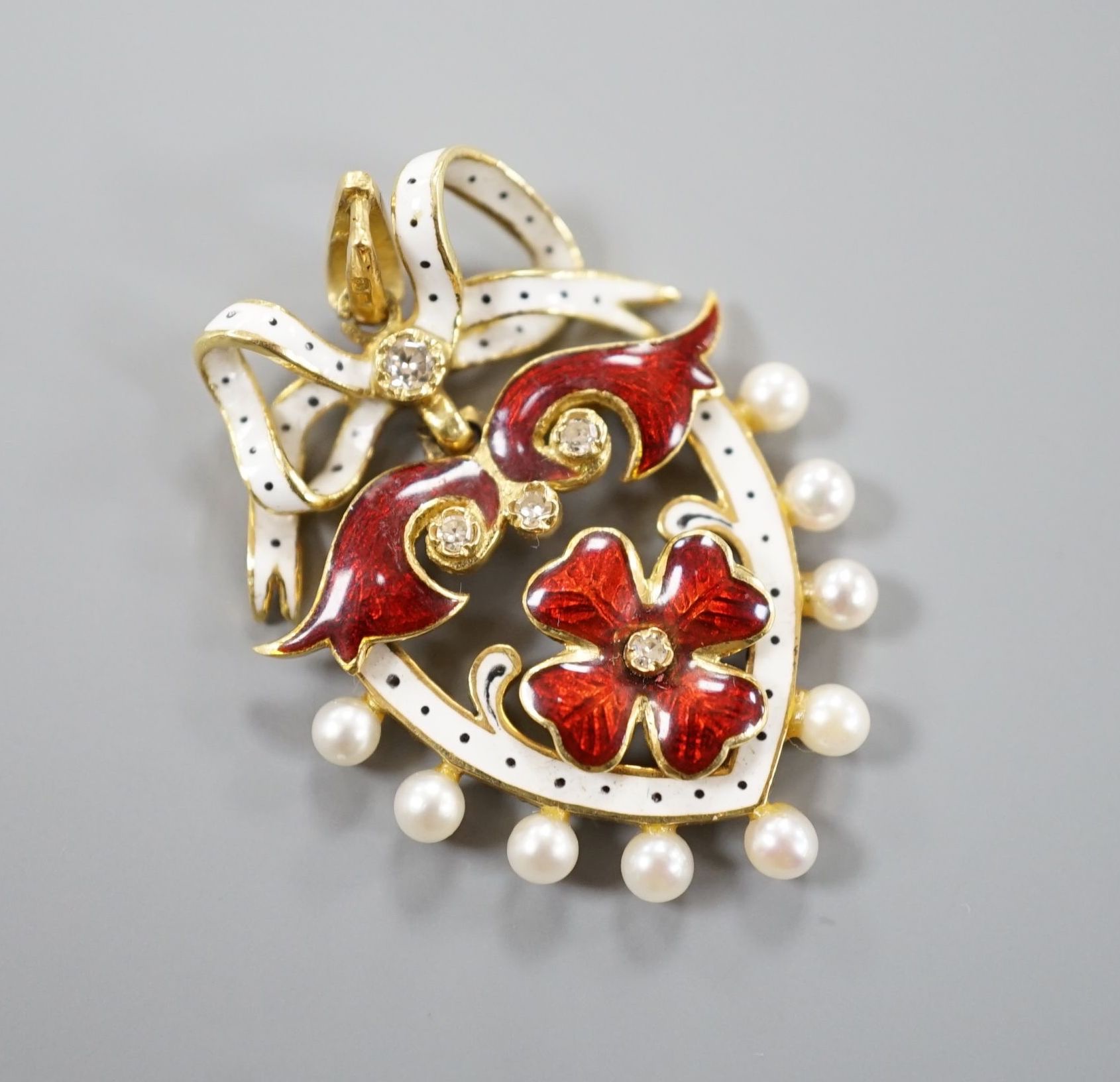 A 1960's 18ct gold, diamond, seed pearl and two colour enamel set heart shaped pendant, with ribbon bow crest, 35mm, gross weight 8.7 grams.